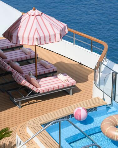 Relax sul ponte di uno yacht della Ritz-Carlton Yacht Collection, con lettini, ombrellone a righe e piscina affacciata sul mare.